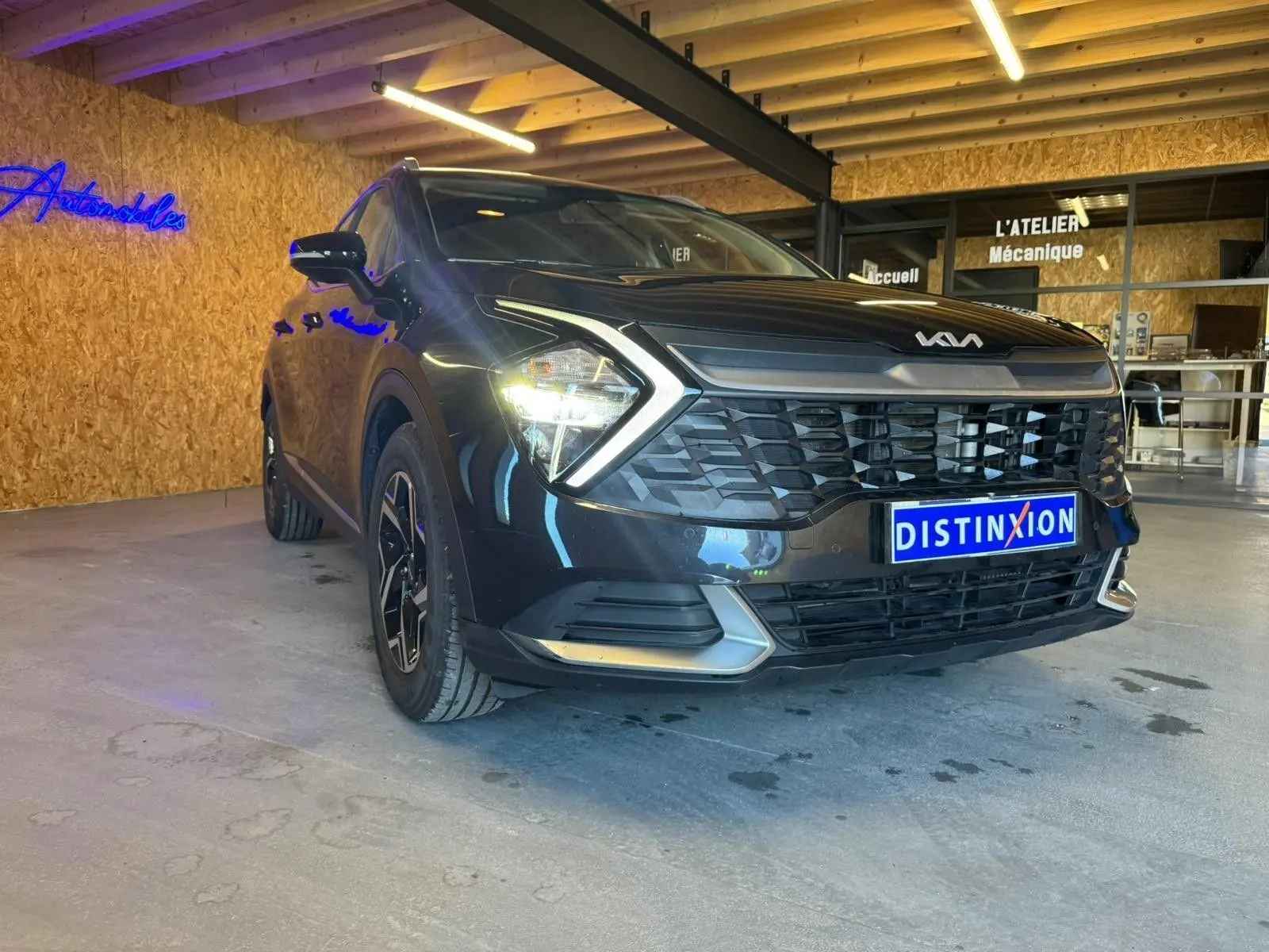 Vue 3/4 avant gauche d’un KIA SPORTAGE noir 2022 avec calandre distinctive et feux allumés en intérieur showroom.
