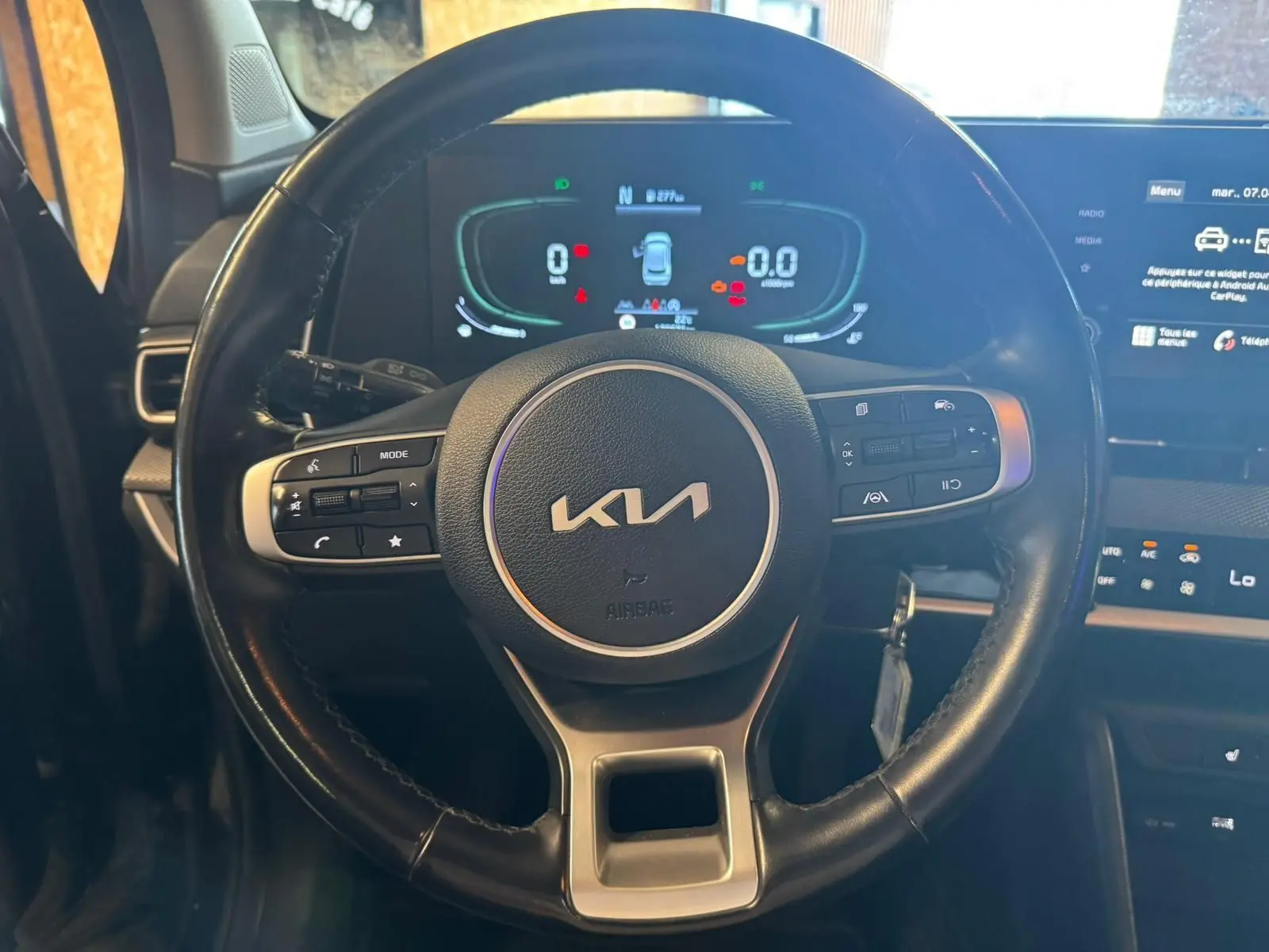 Vue rapprochée du volant noir du Kia Sportage 2022 avec commandes intégrées et tableau de bord numérique éclairé.