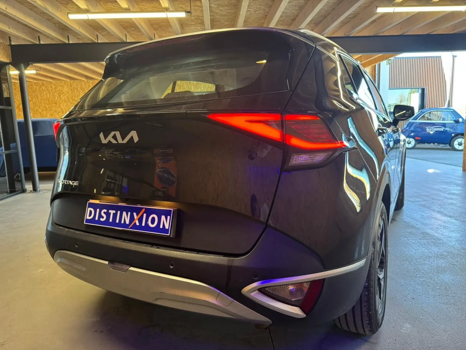Vue 3/4 arrière droite d’un KIA Sportage noir 2022 avec feux arrière allumés et détails chromés sur le pare-chocs.