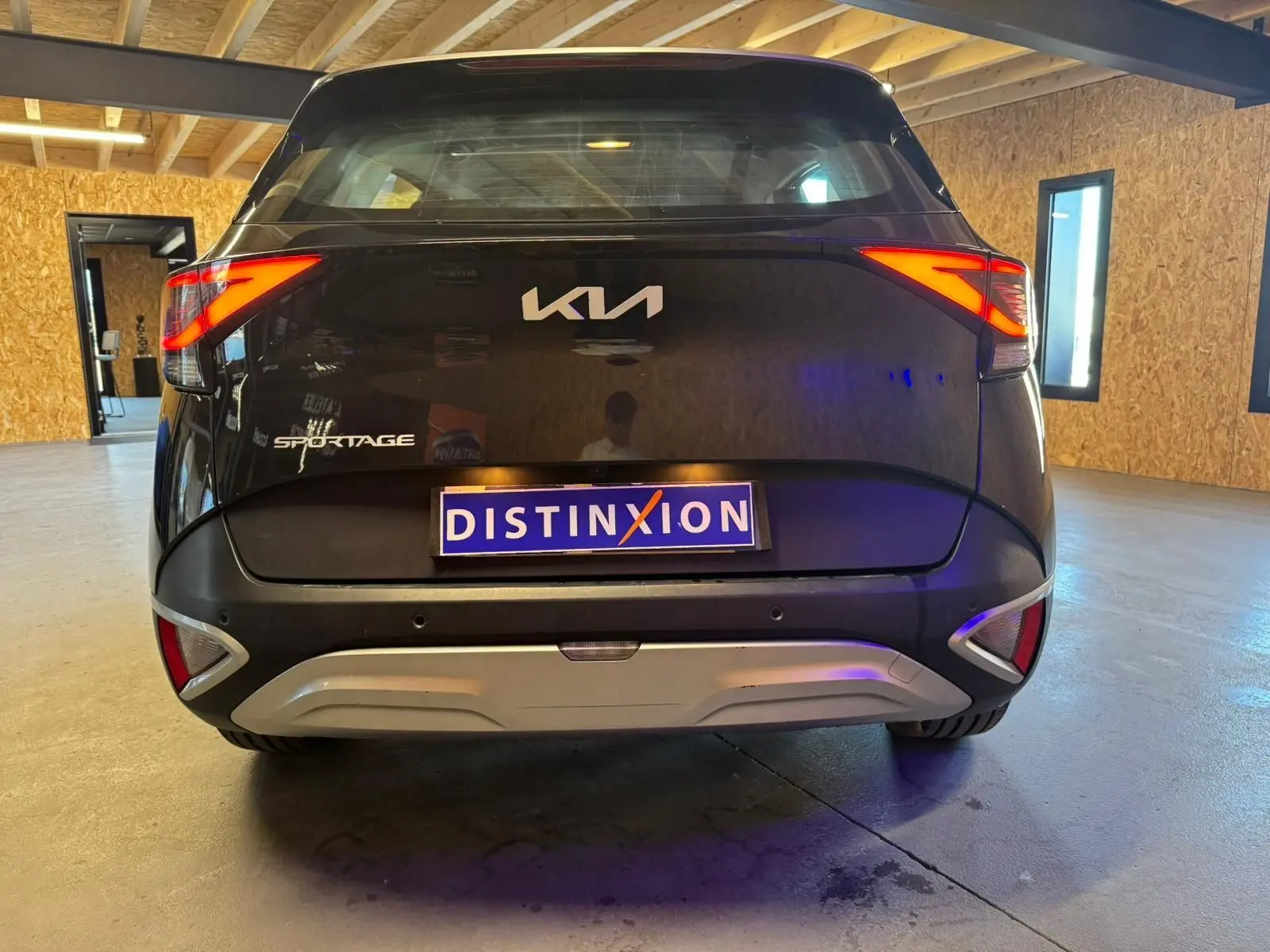 Vue arrière d’un KIA Sportage noir 2022 avec feux arrière allumés et plaque d’immatriculation Distinxion.