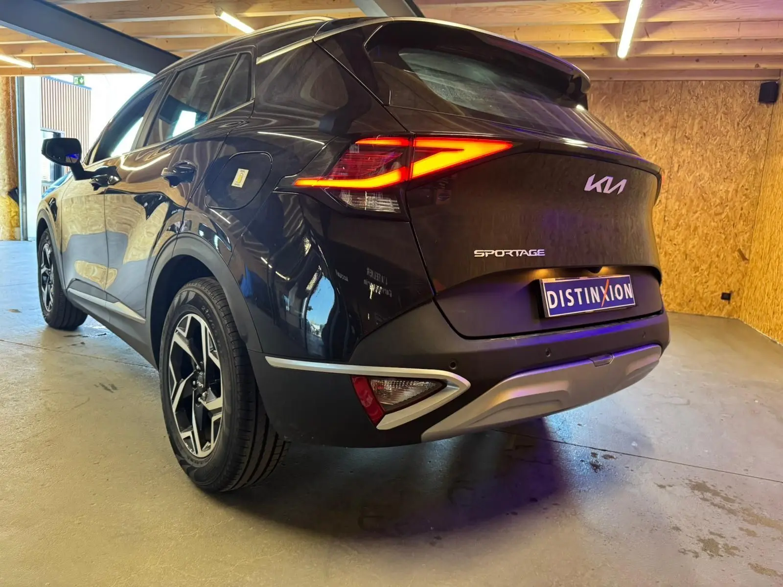 Vue 3/4 arrière droite d'un KIA Sportage noir 2022 avec feux arrière allumés et jantes alliage distinctives.