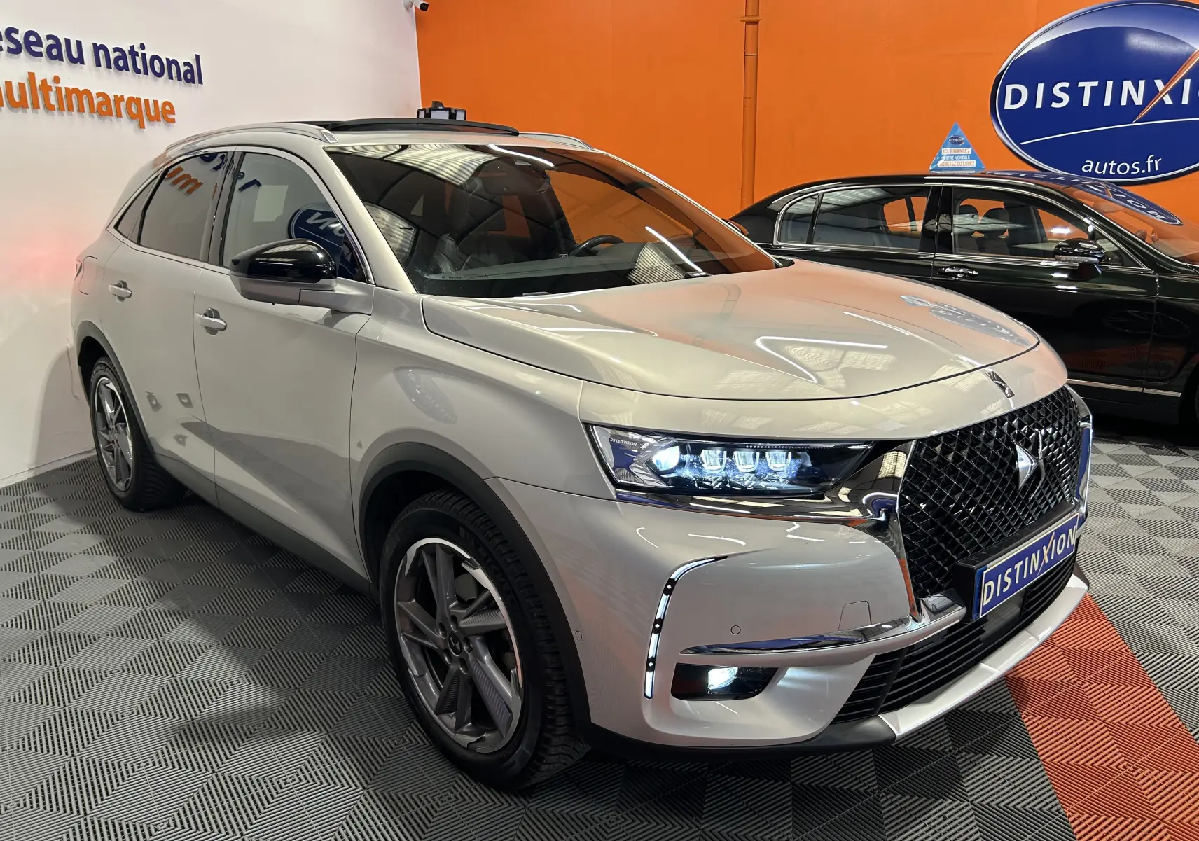 DS7 Crossback bleu clair en 3/4 avant droit, avec calandre distinctive et feux LED allumés dans un showroom.