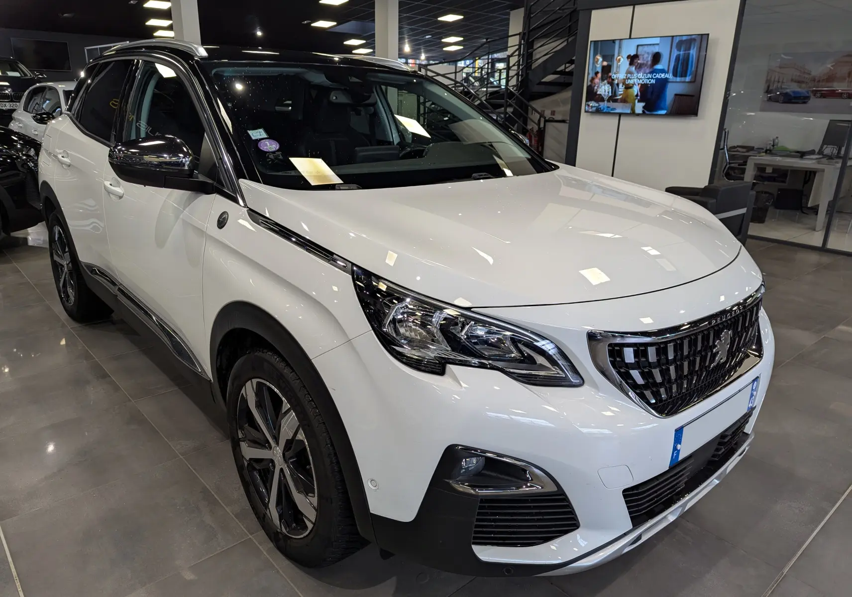 Peugeot 3008 blanc glacier avec toit noir, vue 3/4 avant droit en intérieur de showroom, détails chromés visibles.