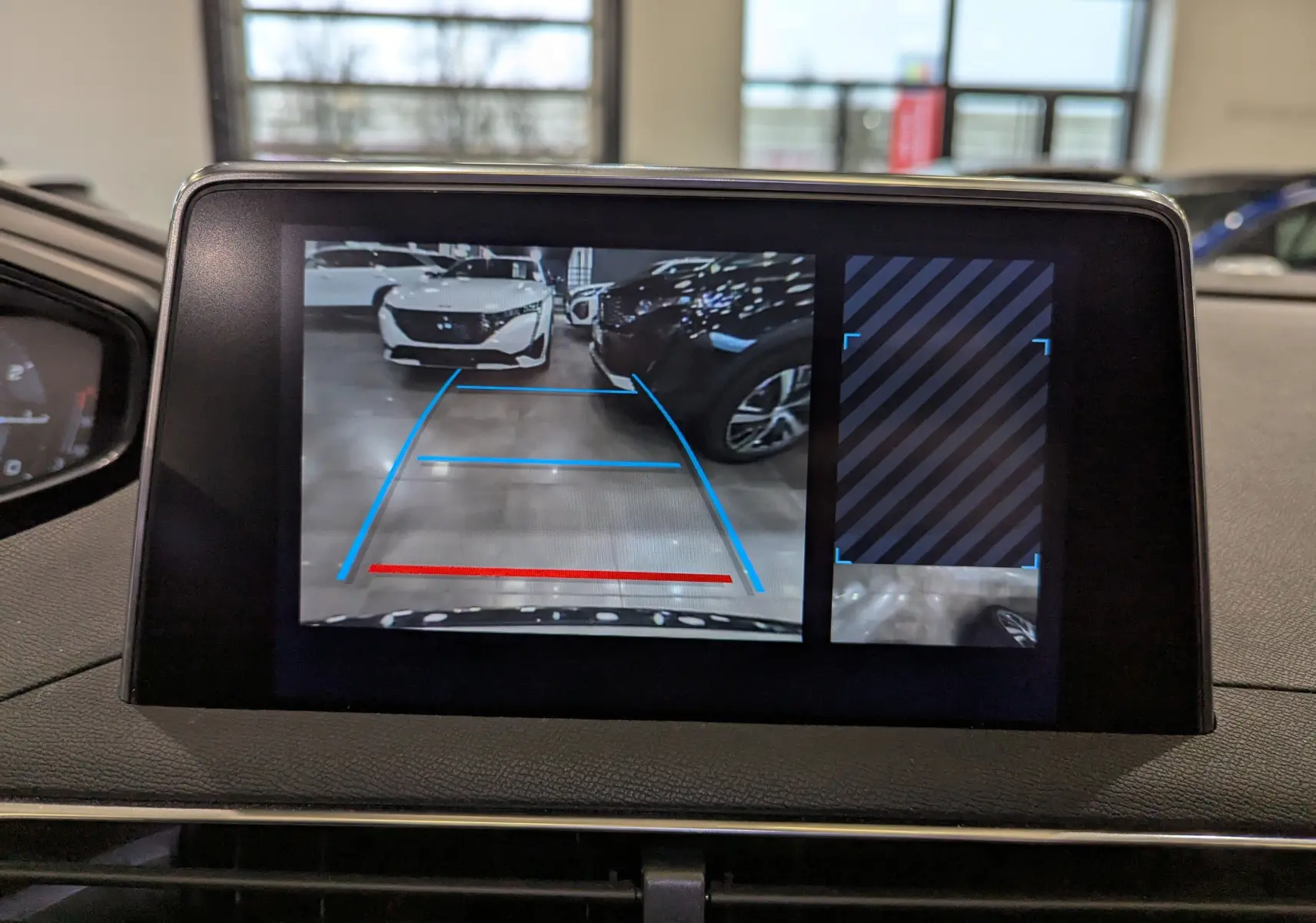 Écran de caméra de recul du Peugeot 3008 blanc Glacier avec toit noir, montrant une voiture garée en face dans un parking intérieur.