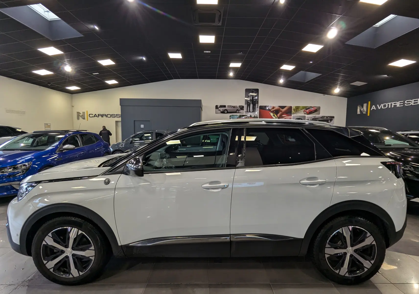 Peugeot 3008 blanc glacier avec toit noir vu de profil côté gauche dans un showroom lumineux.