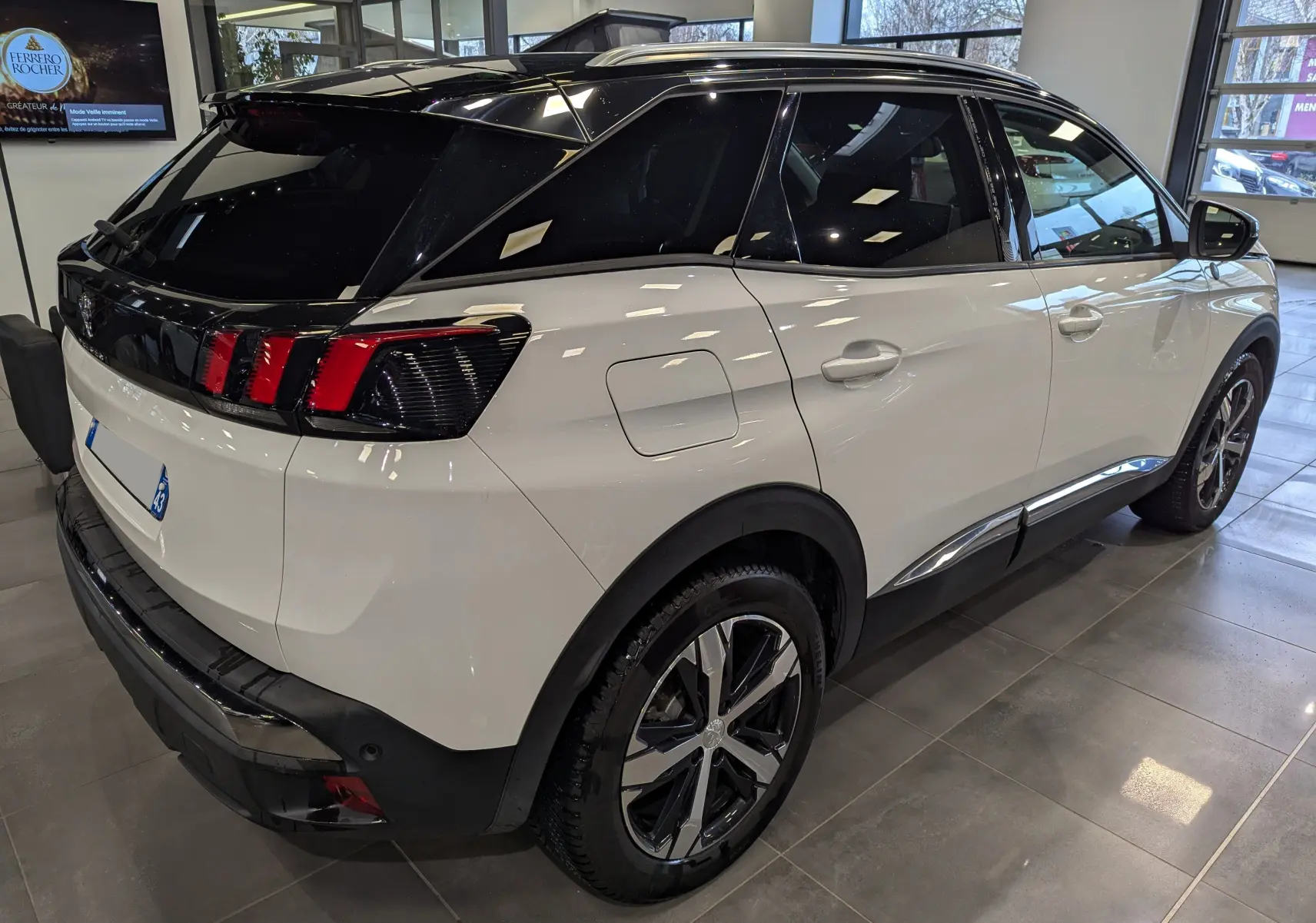 Vue 3/4 arrière droit du Peugeot 3008 blanc Glacier avec toit noir brillant dans un showroom lumineux.
