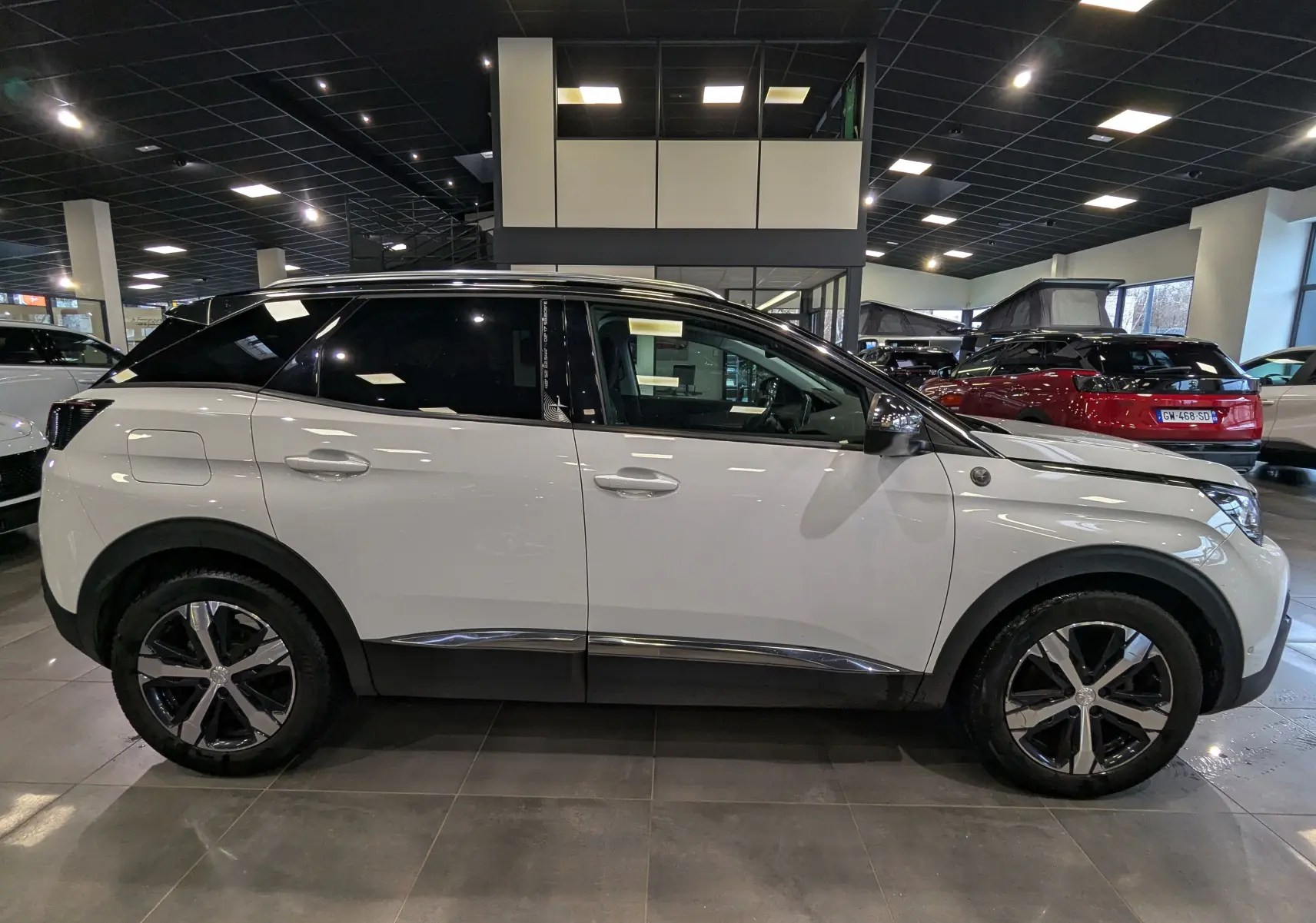 Peugeot 3008 blanc Glacier avec toit noir, vue de profil côté gauche en intérieur de showroom, jantes alliage visibles.