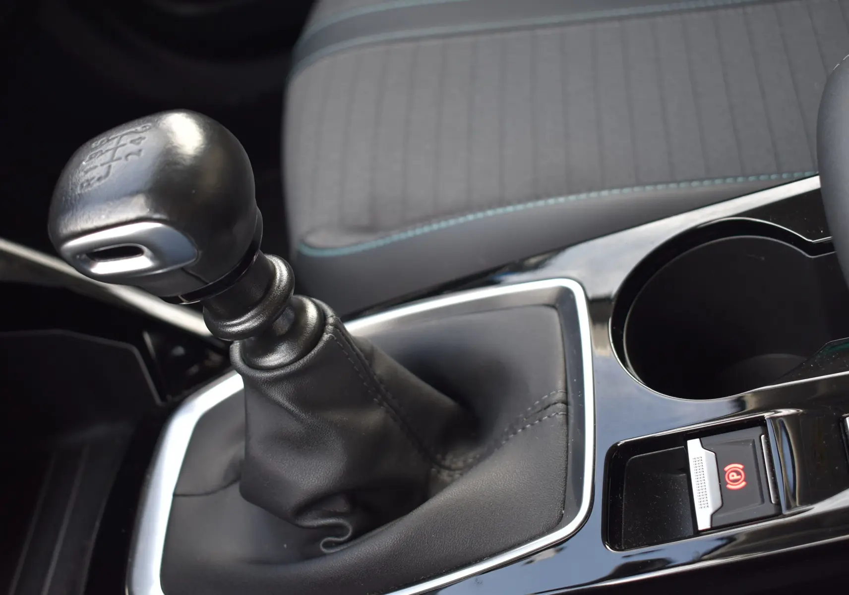 Le levier de vitesses manuel noir du Peugeot 2008 BlueHDi 110, avec siège gris et surpiqûres bleues en arrière-plan.