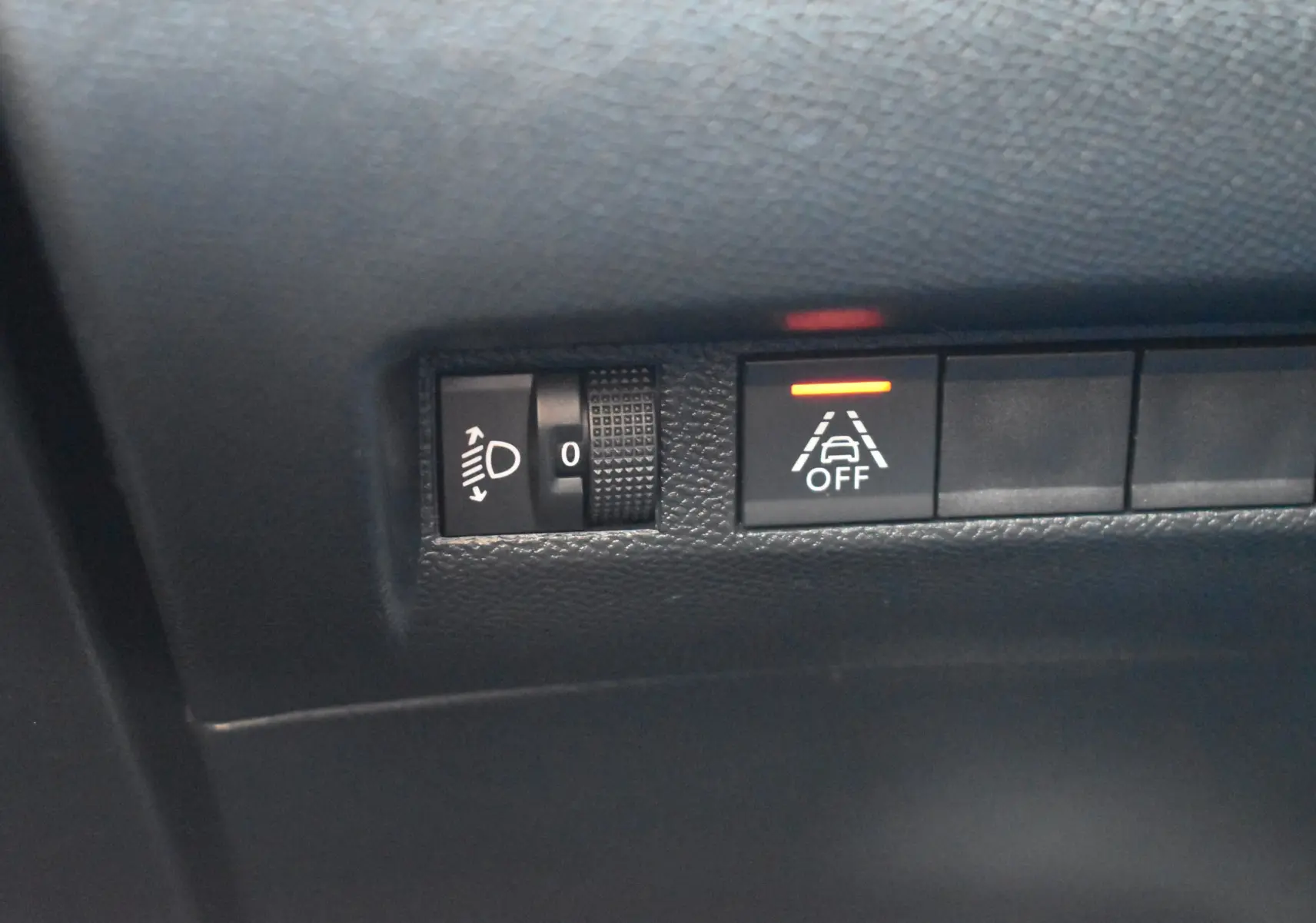 Gros plan sur les commandes de réglage des phares et de désactivation de l'alerte de franchissement de ligne du Peugeot 2008 bleu 2021.