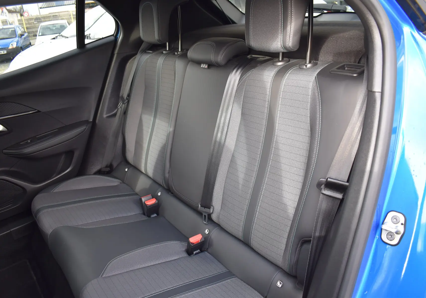 Vue intérieure sur la banquette arrière du Peugeot 2008 bleu 2021, avec sellerie tissu et cuir gris à surpiqûres bleues.