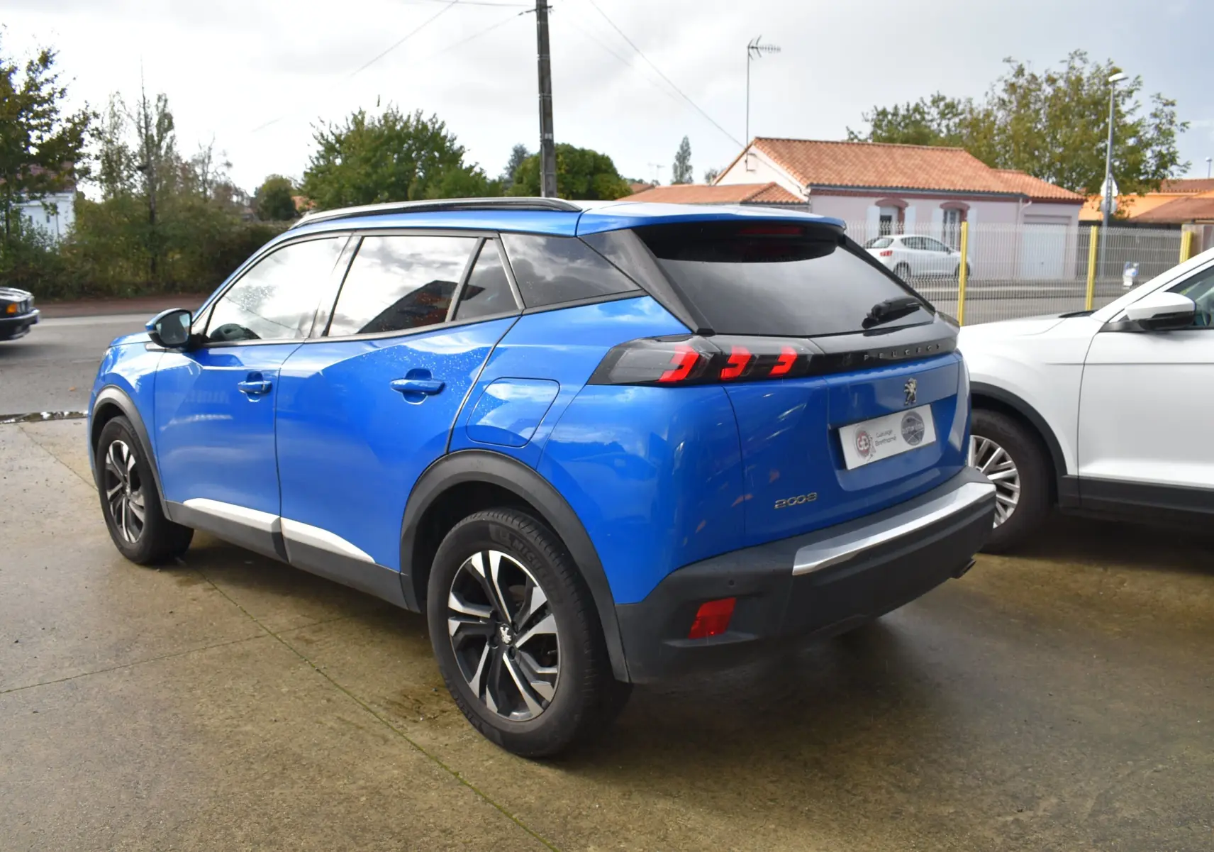 Vue 3/4 arrière droite d'un Peugeot 2008 bleu 2021 avec feux arrière à griffes et jantes alliage noires.