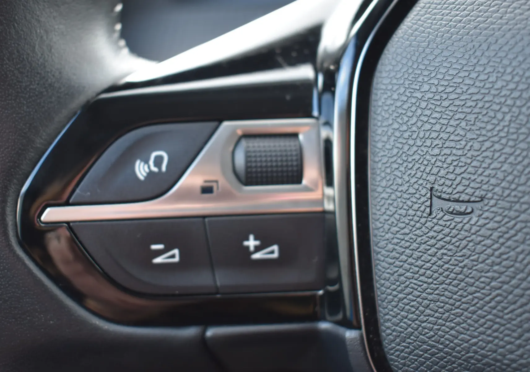 Détail des commandes au volant noir du Peugeot 2008 2021 BlueHDi 110 Allure, avec boutons de volume et micro.