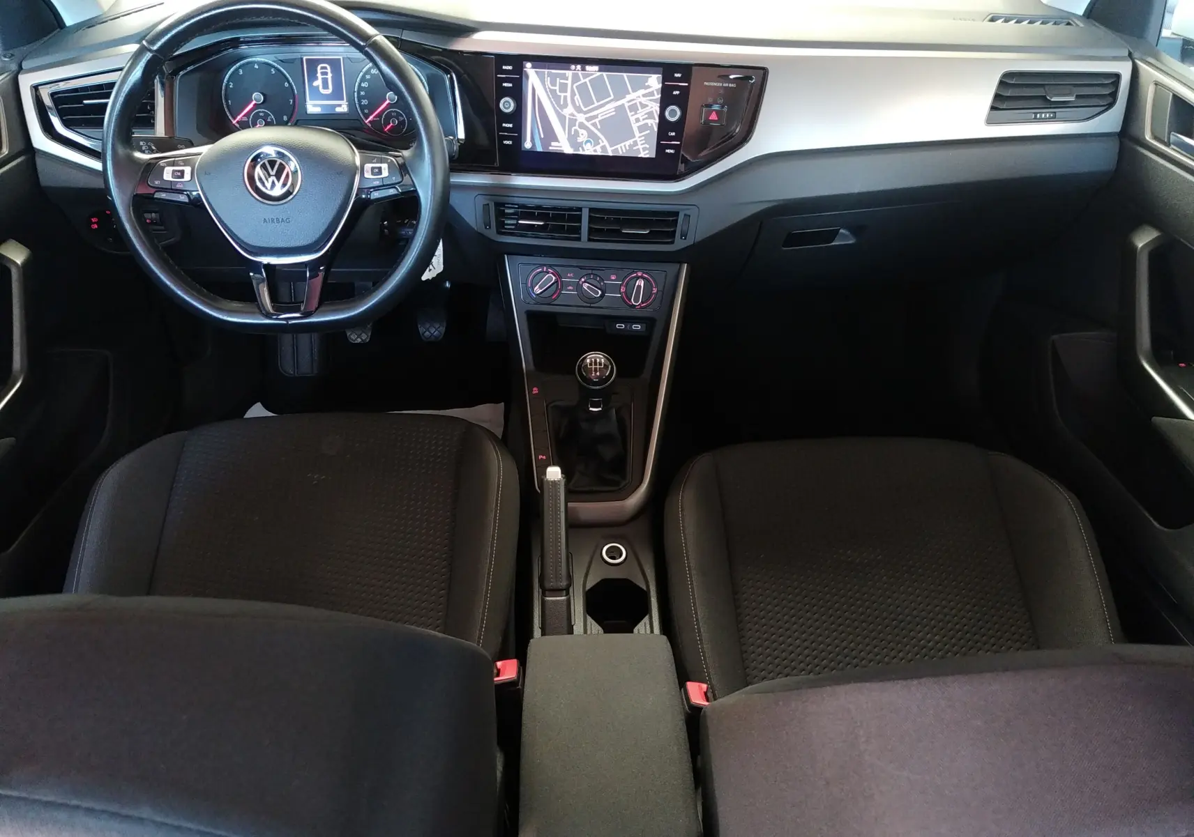 Vue intérieure avant du Volkswagen Polo blanc 2021, tableau de bord avec écran GPS et volant multifonction noir.