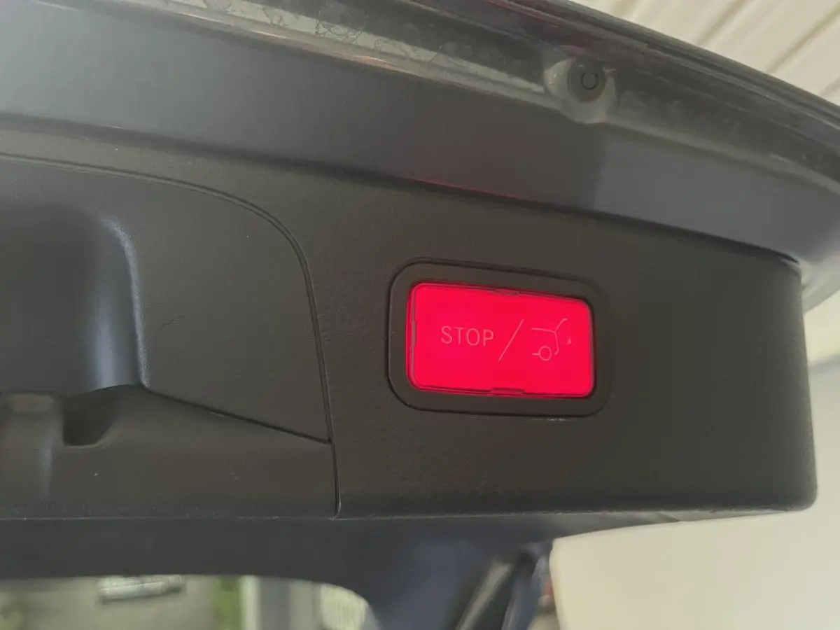 Bouton rouge d'arrêt électrique du hayon visible sous le coffre d'un Mercedes GLC gris, vue rapprochée intérieure.