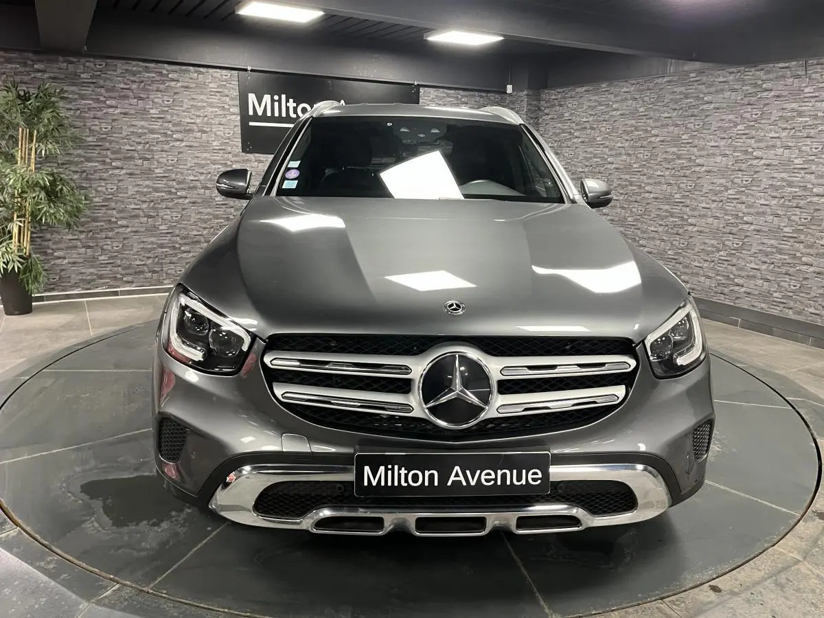 Vue frontale d'un Mercedes GLC gris métallisé exposé en showroom avec calandre chromée et logo étoile central lumineux.