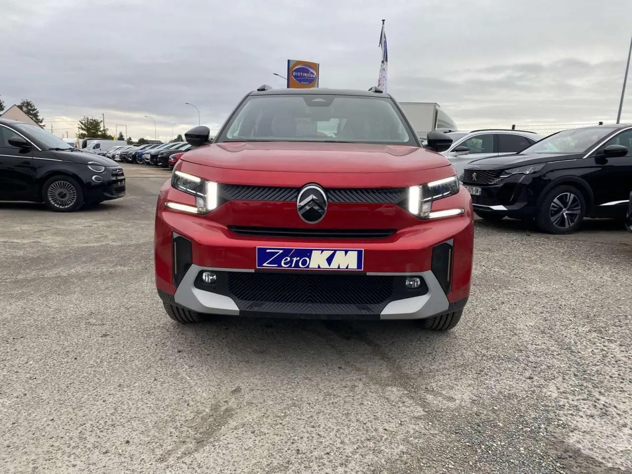 Vue frontale d'un Citroën C3 Aircross 2025 rouge Elixir avec toit noir et feux LED allumés sur parking.