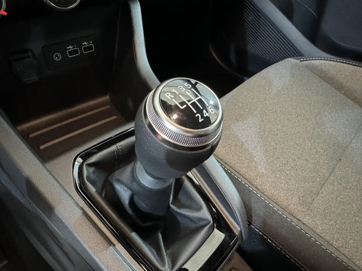 Gros plan sur le levier de vitesses manuel noir de la Renault Clio gris clair, avec sièges tissu visibles à droite.