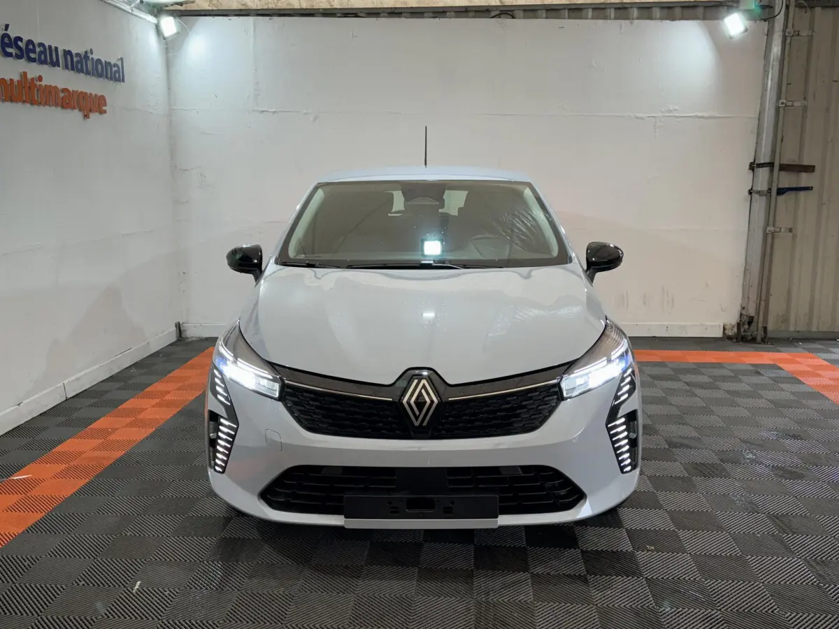 Vue avant d'une Renault Clio gris clair 2025 avec phares LED allumés dans un garage éclairé.