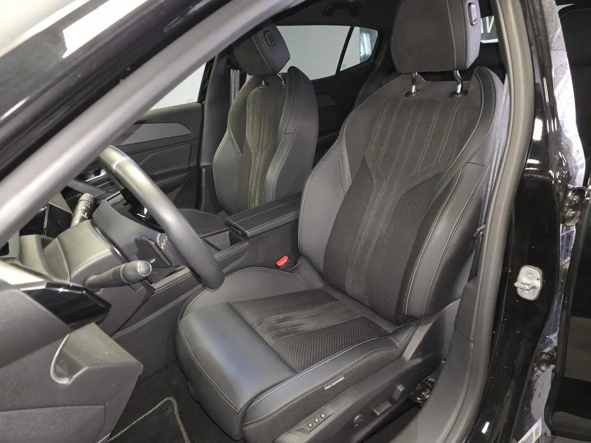 Vue intérieure côté conducteur de la Peugeot 408 GT 1.2i Hybrid 2024, sièges noirs en cuir et tissu avec surpiqûres grises.