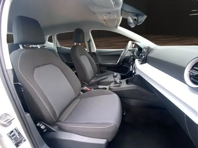 Vue intérieure côté conducteur de la SEAT Ibiza blanche 2023, sièges tissu gris, volant cuir multifonctions et tableau de bord moderne.