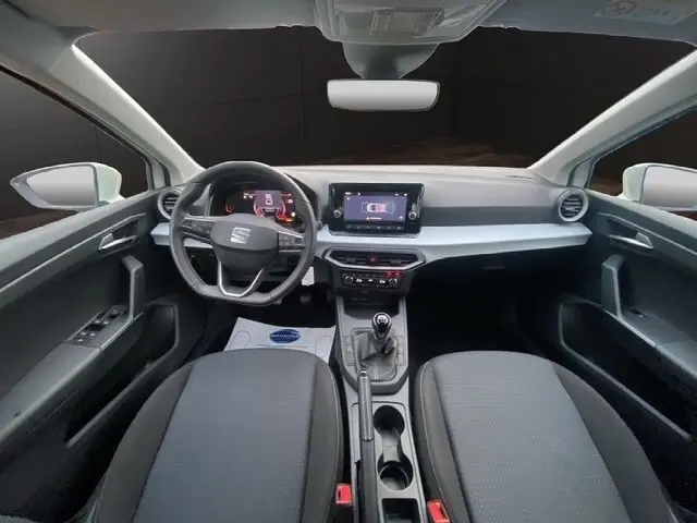 Vue intérieure avant de la SEAT Ibiza blanche 2023, volant cuir multifonctions et écran tactile central visible.