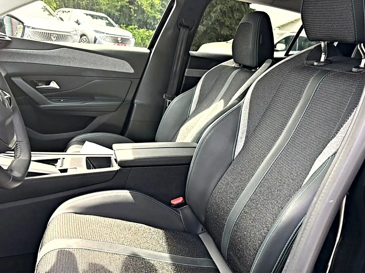 Vue intérieure côté gauche de la Peugeot 408 Hybrid 136 allure 2024, sièges tissu et cuir noir avec accoudoir central.