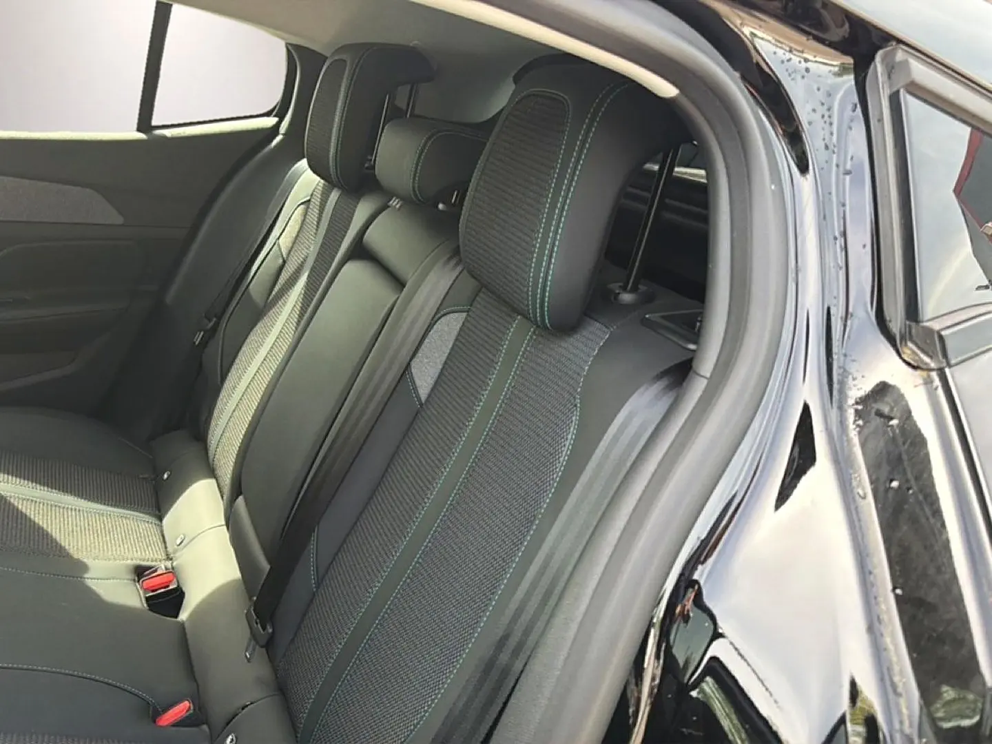 Vue intérieure côté arrière droit d’une Peugeot 408 noire, montrant la banquette arrière en tissu avec surpiqûres contrastantes.