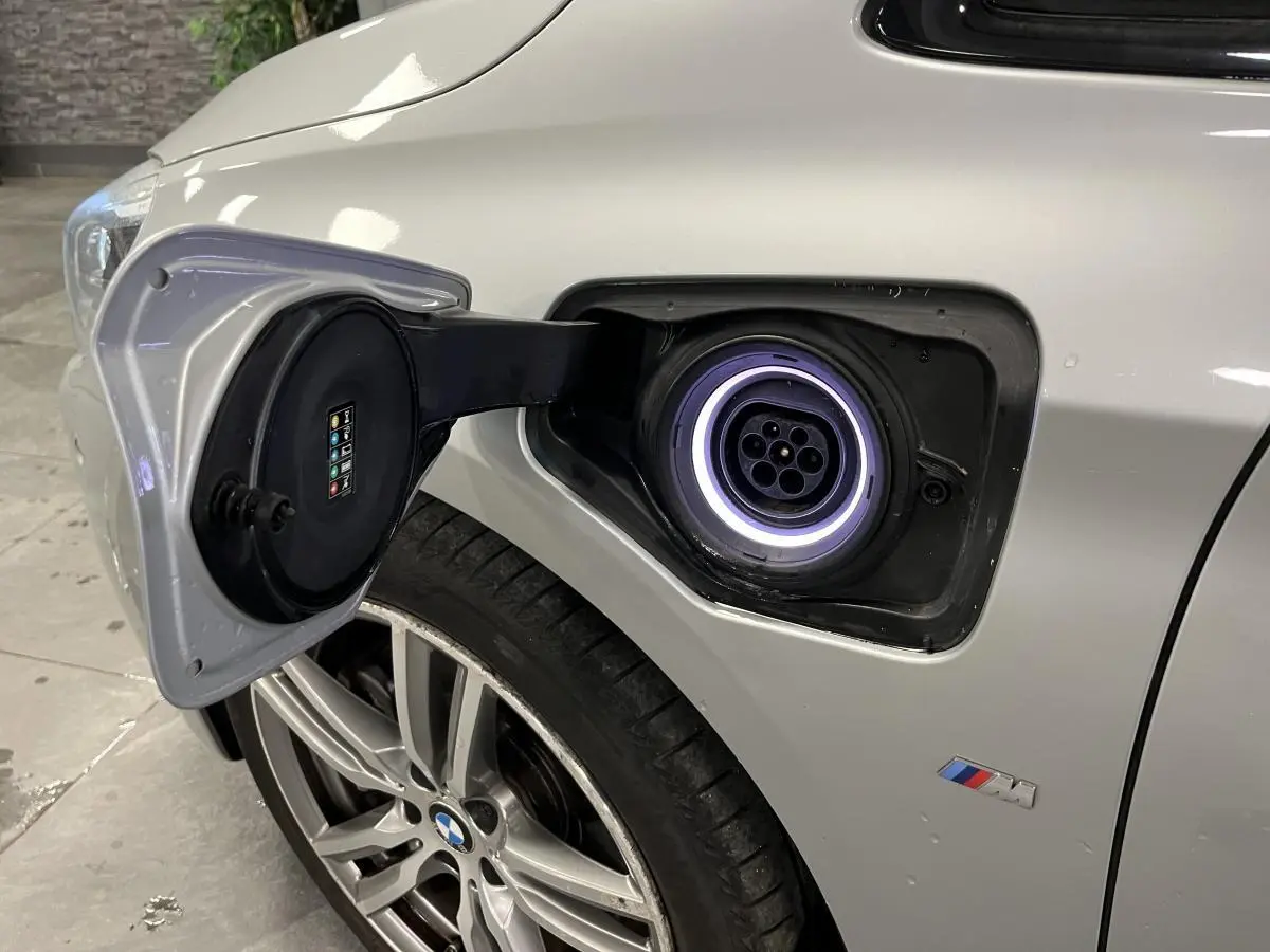 Prise de recharge ouverte côté avant gauche sur BMW Série 2 gris avec jante alliage et badge M visible.