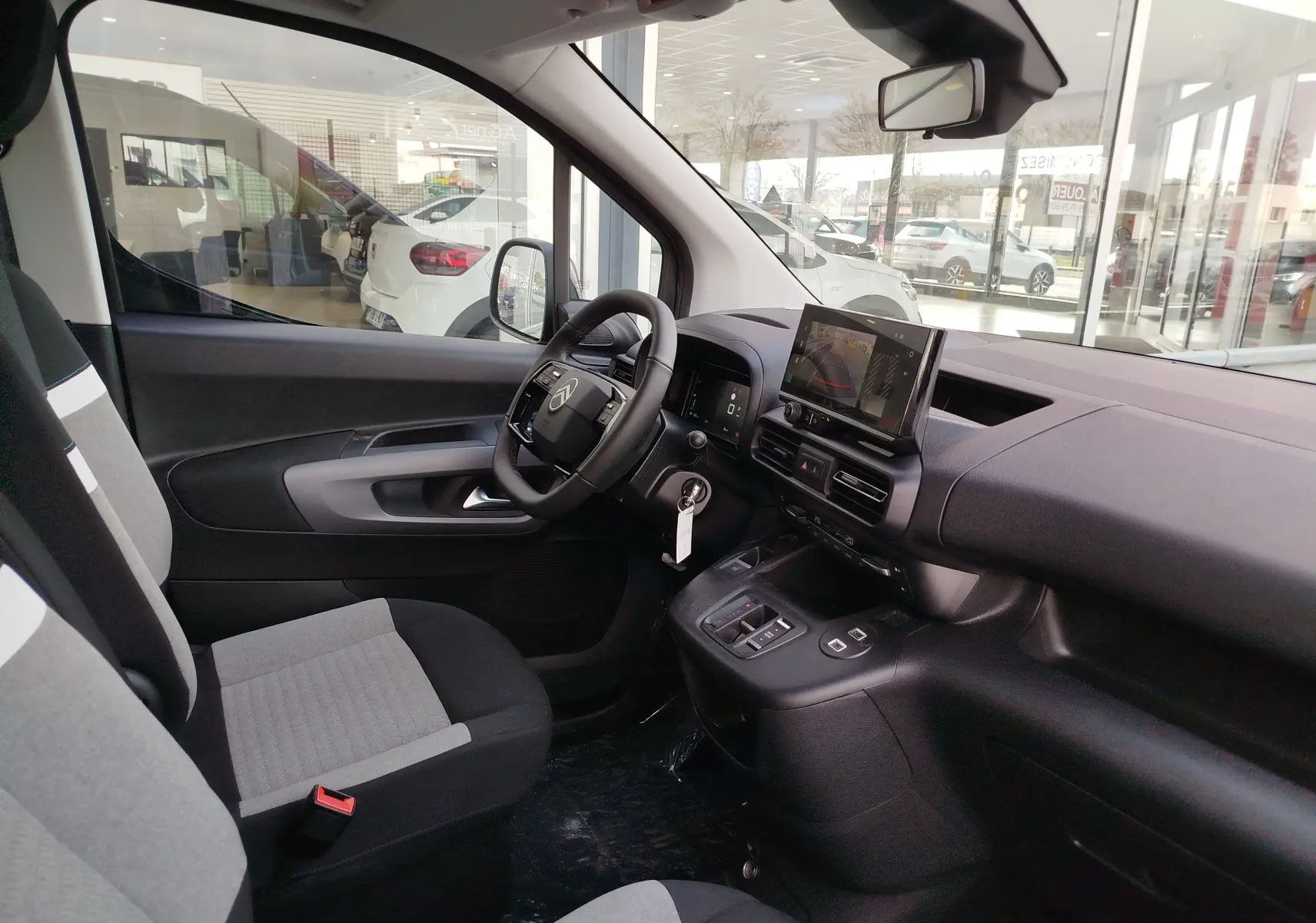 Vue intérieure côté conducteur du Citroën Berlingo 2025, sièges gris, tableau de bord avec écran tactile et volant multifonction.