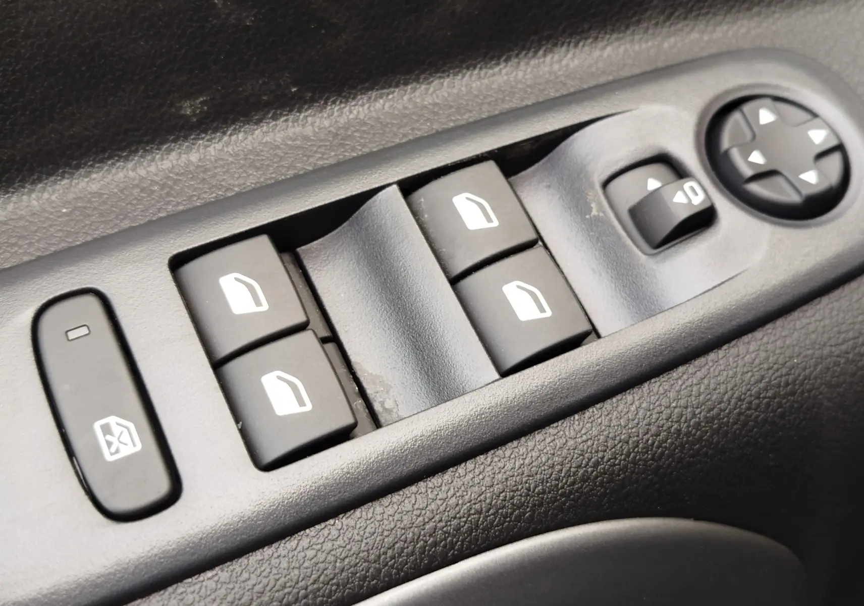 Détail des commandes de lève-vitres et réglage des rétroviseurs sur la porte côté gauche d’un Citroën Berlingo bleu Kiarma.