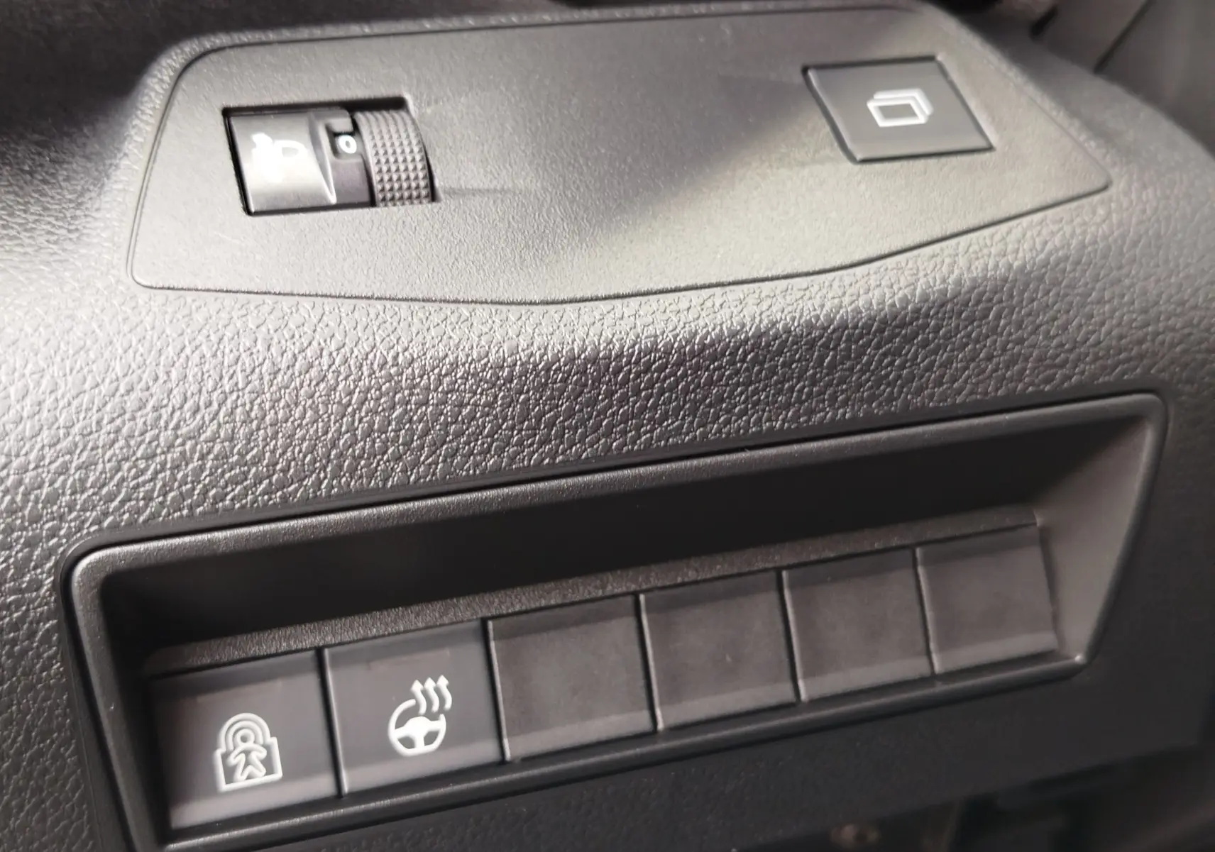 Gros plan sur les commandes noires du tableau de bord du Citroën Berlingo 2025, avec bouton de verrouillage et volant chauffant.