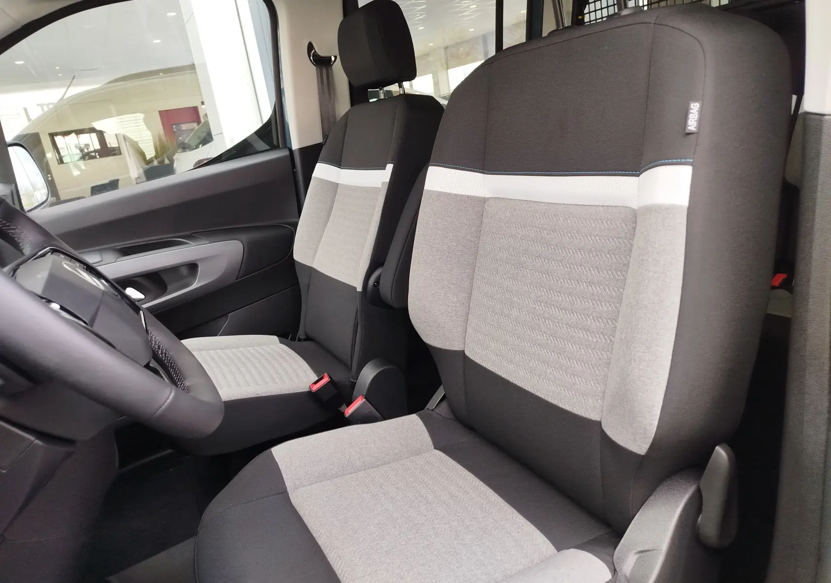 Vue intérieure côté conducteur du Citroën Berlingo 2025, sièges tissu gris et noir avec détails blancs et bleu.