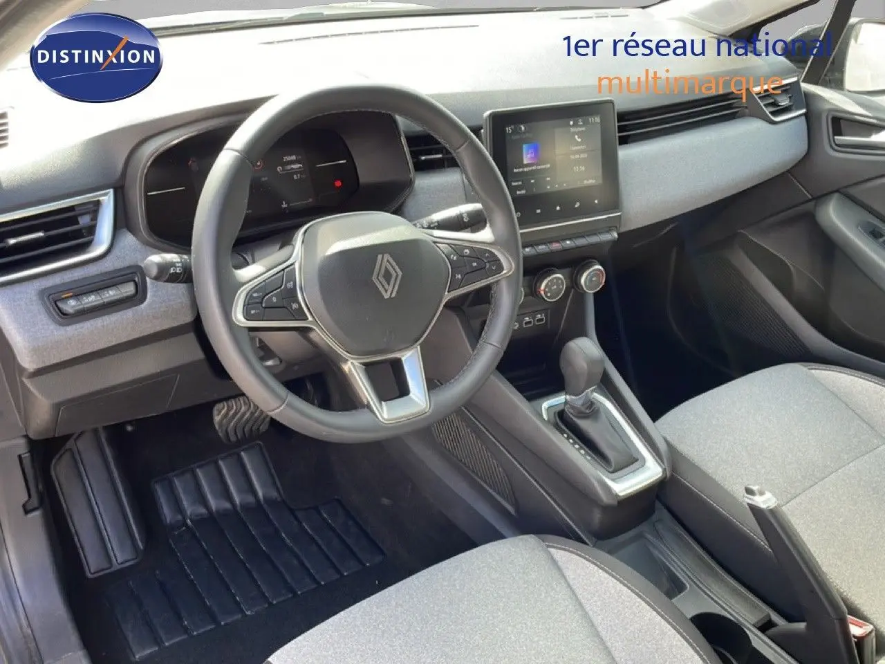 Vue intérieure de la Renault Clio 2025, tableau de bord et volant noir avec sellerie tissu gris clair.