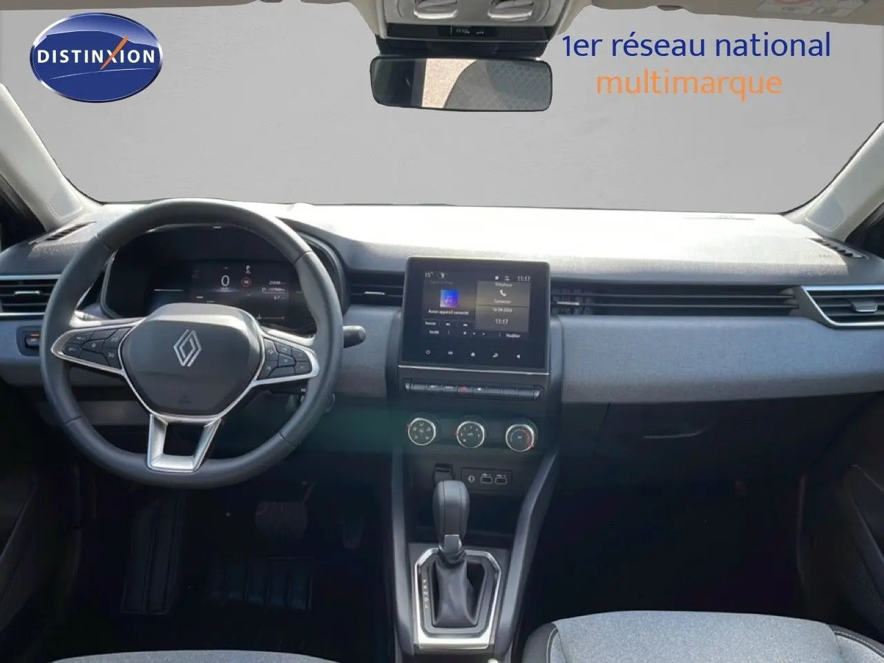Vue intérieure avant de la Renault Clio 2025, tableau de bord gris clair avec écran tactile central et volant multifonction noir.