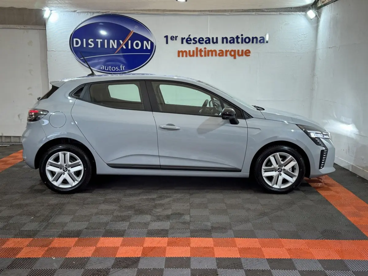 Profil droit d'une Renault Clio gris clair Evolution Blue dCi 100 2025, en intérieur avec logo Distinxion en arrière-plan.