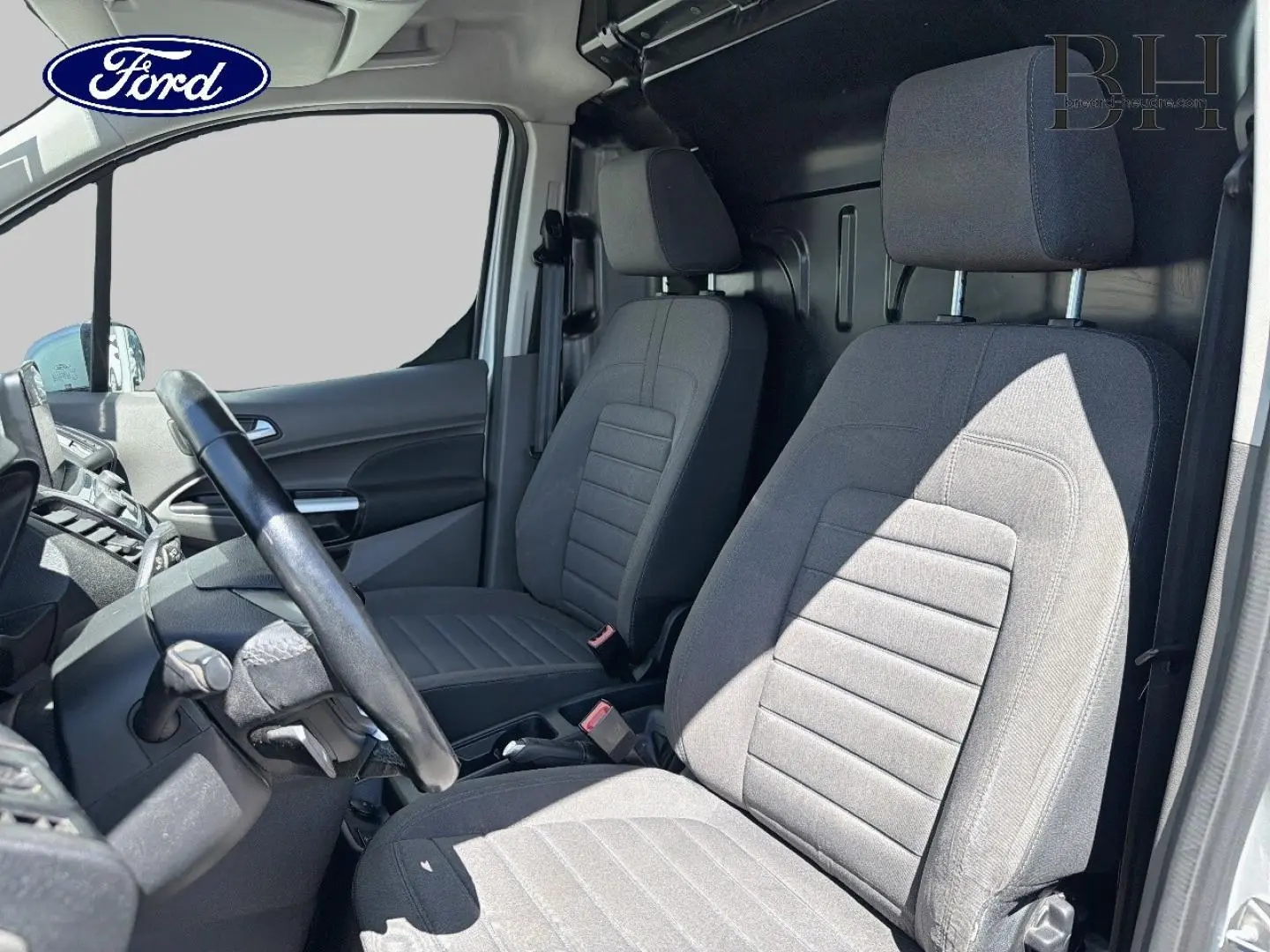 Vue intérieure côté conducteur du Ford Transit Connect gris, montrant les sièges avant et le volant multifonction.