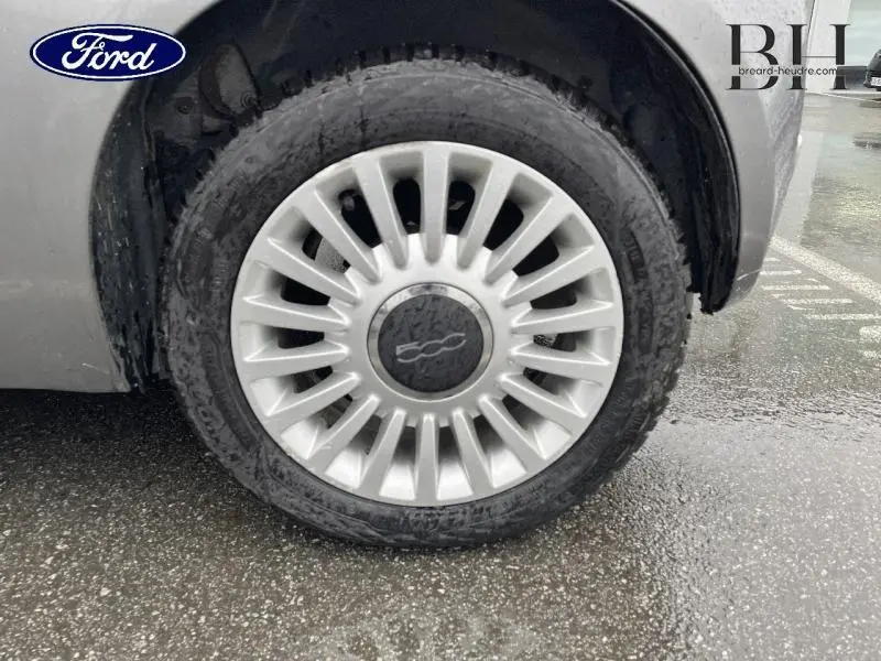 Gros plan sur la roue avant gauche d'une Fiat 500 marron avec jante alu caractéristique et logo central visible.