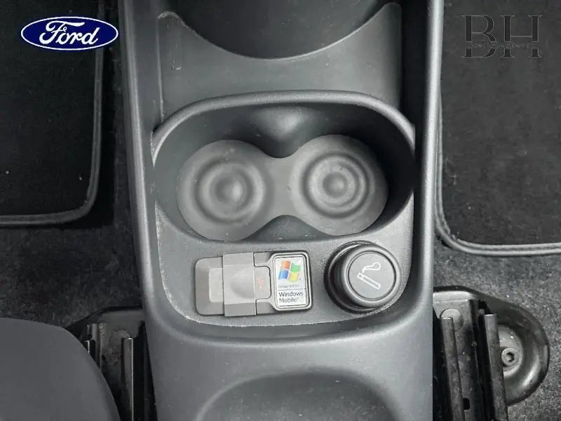 Vue plongeante sur la console centrale noire d'une Fiat 500 marron, avec porte-gobelets et allume-cigare visible.