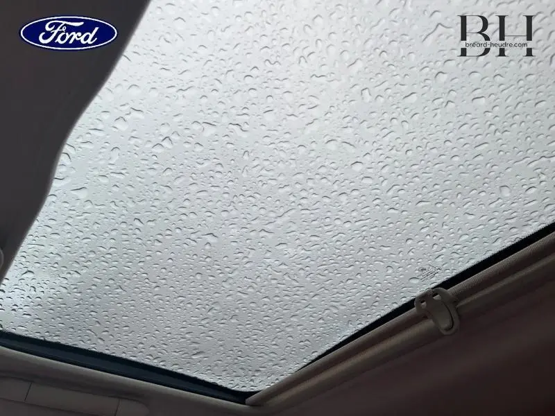 Toit panoramique en verre de Fiat 500 marron vu de l'intérieur avec gouttes de pluie sur la surface vitrée.