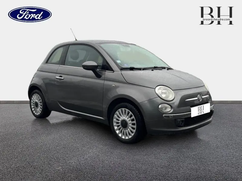 Vue 3/4 avant droite d'une FIAT 500 marron métallisé de 2010 avec jantes alu et toit ouvrant électrique visible.