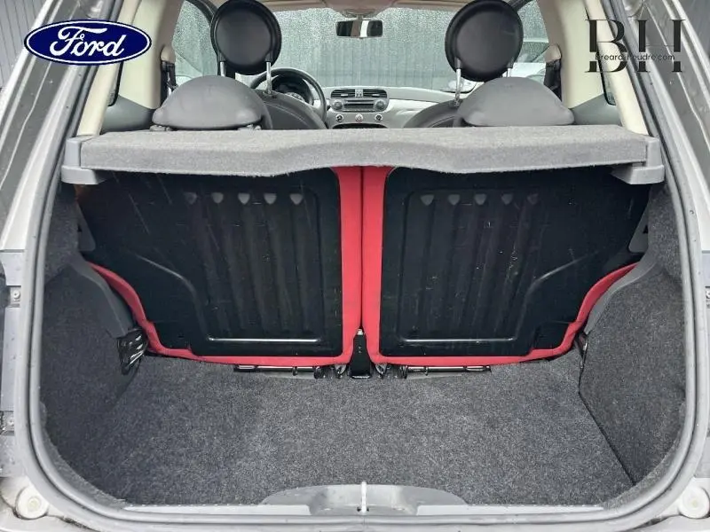 Vue arrière du coffre ouvert d'une FIAT 500 marron, montrant la banquette arrière noire avec contours rouges et l'intérieur du véhicule.