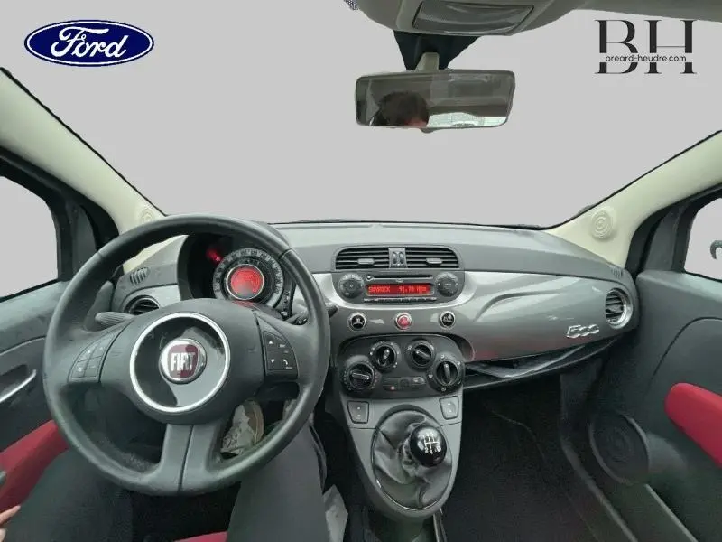 Vue intérieure avant centrée sur le tableau de bord gris brillant et volant noir de la Fiat 500 avec levier de vitesse manuel.