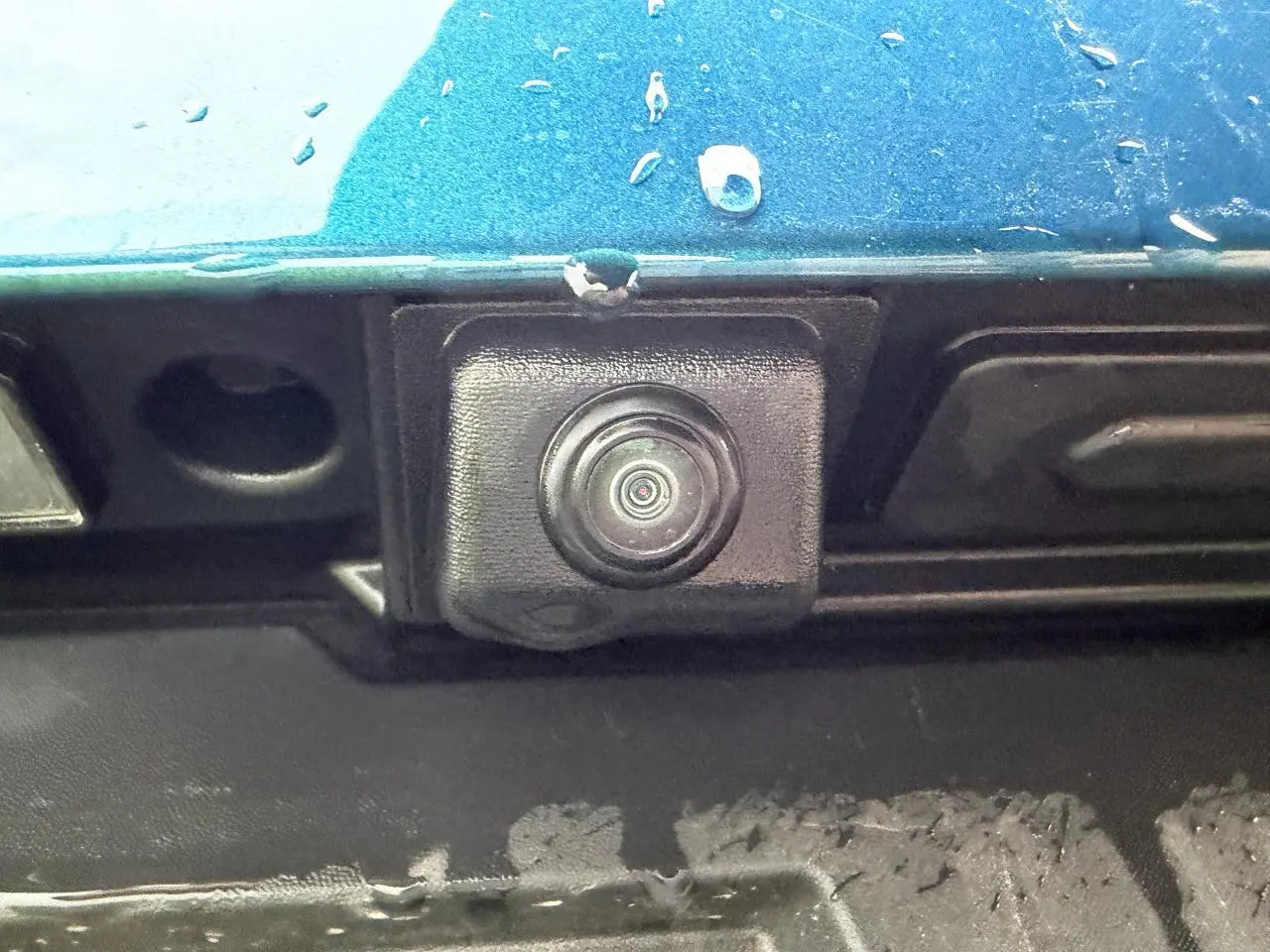 Gros plan sur la caméra de recul noire intégrée dans la partie arrière bleu Zanzibar métallisé du Renault Arkana 2025.