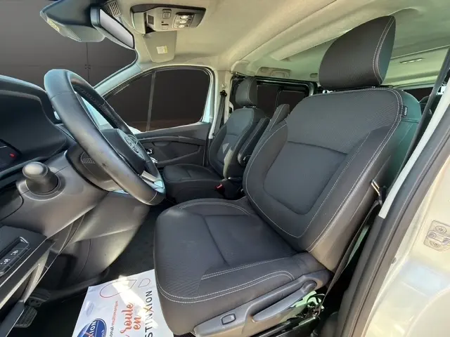 Vue intérieure côté conducteur du Nissan Primastar gris clair 2025, mettant en valeur les sièges noirs et le volant multifonctions.