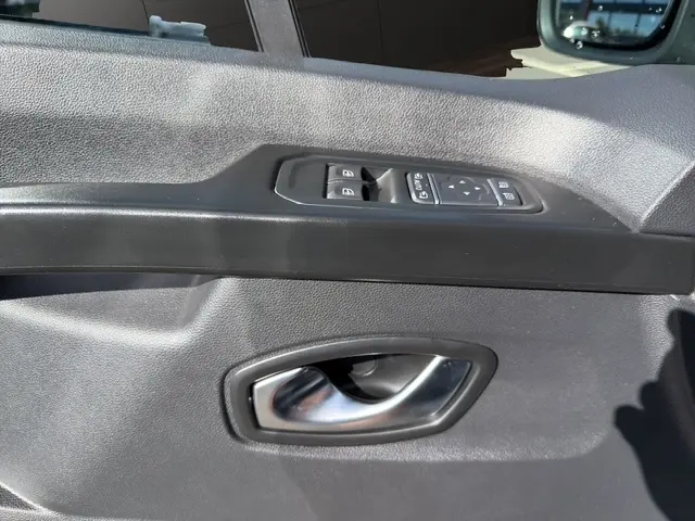 Gros plan sur la poignée intérieure et les commandes électriques de la porte côté conducteur du Nissan Primastar gris clair.