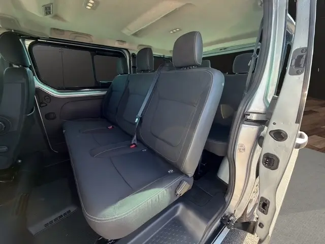 Vue intérieure côté droit sur la banquette arrière noire du Nissan Primastar gris clair avec porte latérale ouverte.