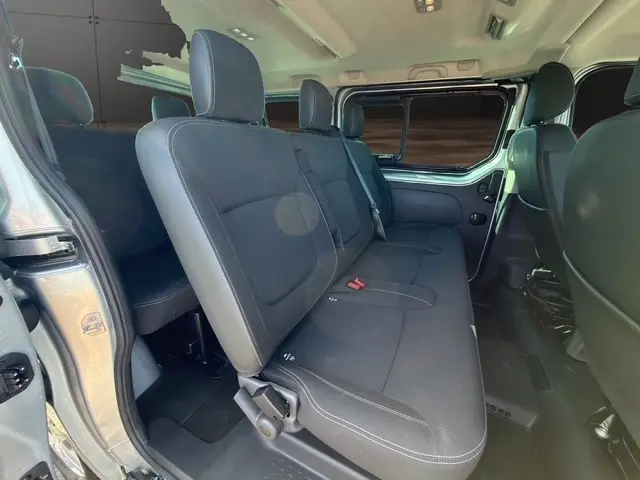 Vue intérieure côté droit sur la banquette arrière noire du Nissan Primastar gris clair avec porte latérale ouverte.