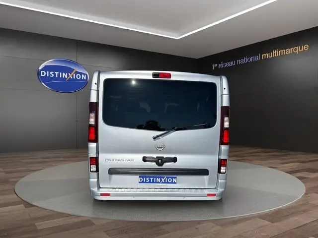 Vue arrière d'un Nissan Primastar gris clair 2025, avec vitres teintées et feux arrière verticaux allumés.