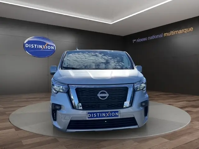 Vue de face d'un Nissan Primastar gris clair, avec calandre noire et logo Nissan bien visible, dans un showroom.