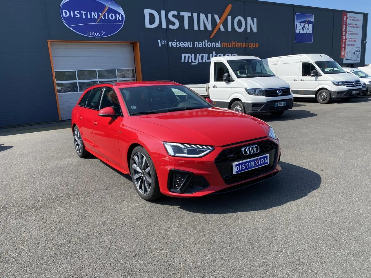 Audi A4 Avant S line rouge Tango vue 3/4 avant droit sur parking devant un bâtiment Distinxion.